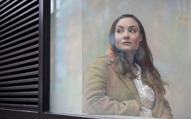 A women looks out a window with a serious expression.